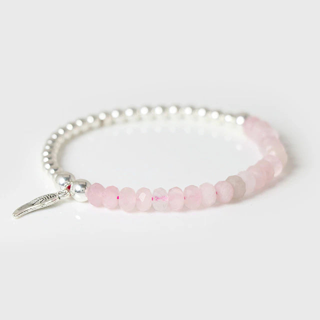 A bracelet with pink beads and silver-colored metal beads, featuring a small angel wing charm, displayed against a white background.
